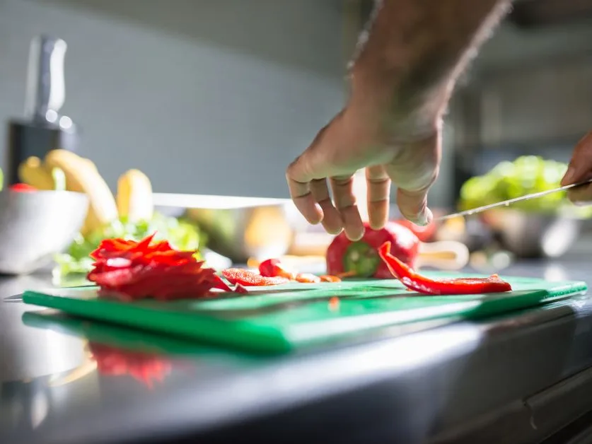 Mains qui coupent un poivron rouge sur une planche